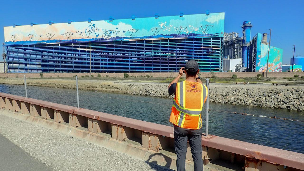 一名工全球最大体育平台戴着帽子，穿着安全背心，沿着河道拍摄海水淡化厂的照片